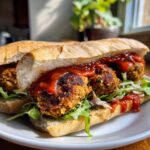 Close-up of Homemade Vegan Chickpea Quinoa Meatball Subs loaded with sauce and greens on a white plate.