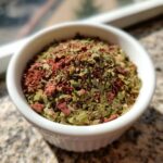 Close-up of a small white bowl filled with a vibrant Italian Seasoning Easy Homemade Blend, showing green dried herbs and red spice flakes.