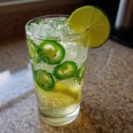 Close-up of a tall glass filled with a bubbly Jalapeno Lemon Lime Mocktail, ice, and slices of jalapeno.