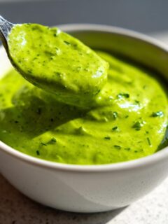 Close-up of a spoonful of bright green Jalapeno Ranch Sauce Dairy Free being lifted from a small white bowl.