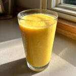 A tall glass filled with a bright yellow Jamaican Pineapple Smoothie, showing condensation on the glass.
