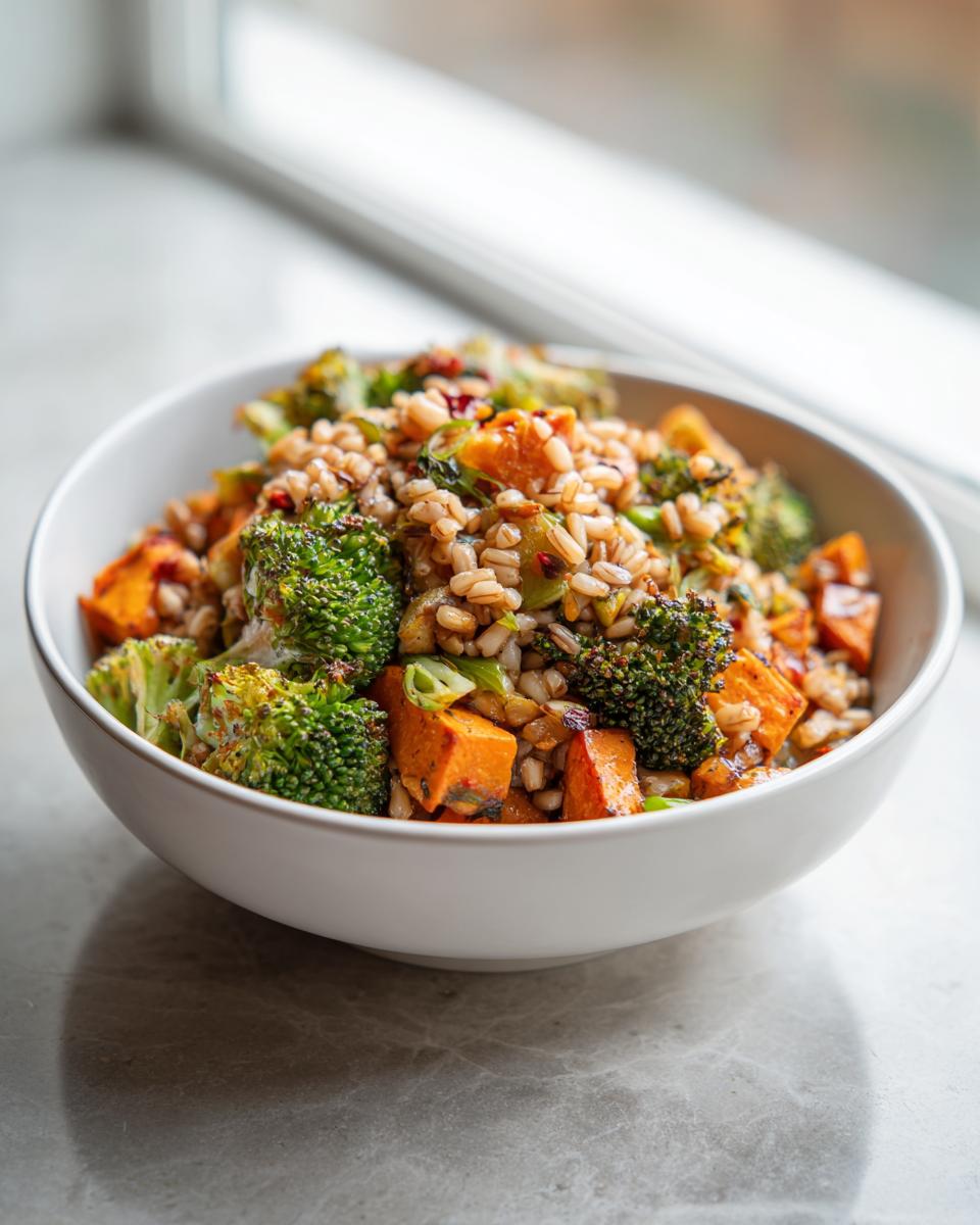 A white bowl filled with Jerk Vegetable Farro Bowl featuring roasted sweet potatoes, broccoli florets, and seasoned farro.