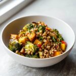 Close-up of a white bowl filled with Jerk Vegetable Farro Bowl featuring farro, roasted broccoli, and squash.