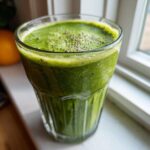 Close-up of a vibrant green Lemon Ginger Detox Smoothie topped with chia seeds in a textured glass.