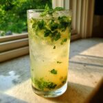 A tall, frosty glass filled with a Lemon Honey Mint Mocktail, muddled with fresh mint leaves and ice.