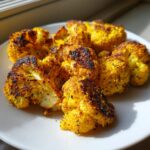 Crispy, golden-yellow Lemon Pepper Cauliflower Bites seasoned with black pepper, served on a white plate.