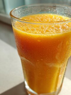Close-up of a tall, frosty glass filled with a vibrant orange Mango Papaya Smoothie, condensation visible on the exterior.