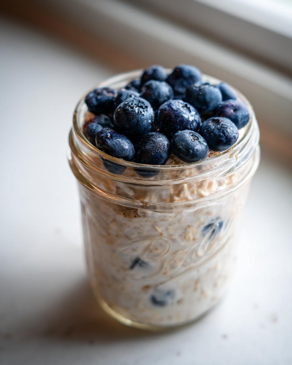 Close-up of Maple Cinnamon Overnight Oats in a glass jar, topped generously with fresh blueberries.