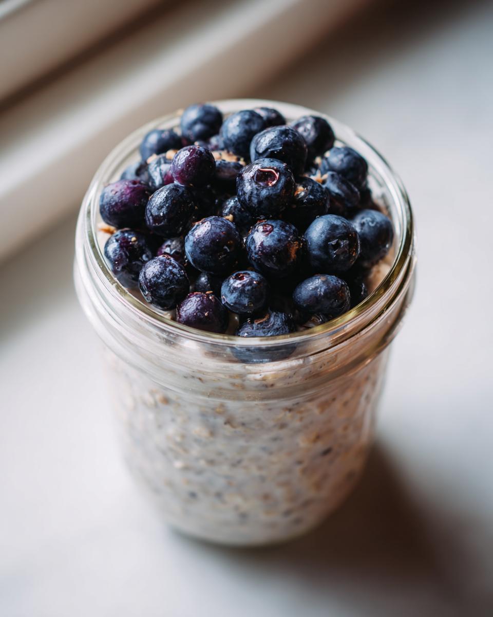 Close-up of Maple Cinnamon Overnight Oats topped generously with fresh, dark blueberries in a glass jar.