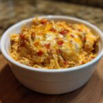 A close-up of a white bowl filled with creamy Mexican Style Chicken Queso Dip topped with melted cheese and diced tomatoes.