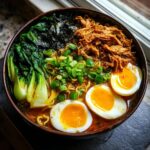 Overhead view of a rich bowl of Nourishing Homemade Chicken Ramen topped with shredded chicken, bok choy, and soft-boiled eggs.
