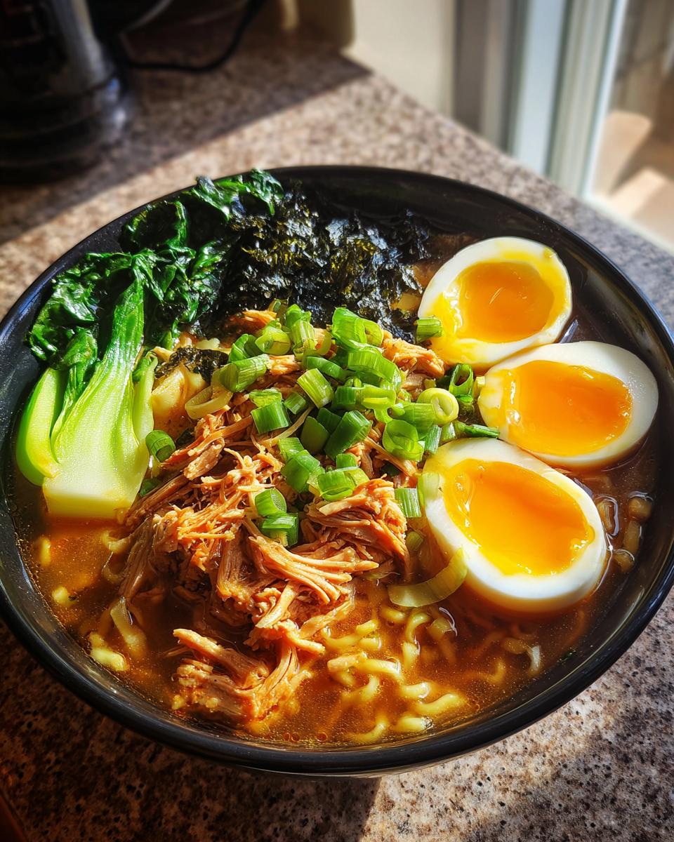 A close-up of a bowl of Nourishing Homemade Chicken Ramen topped with shredded chicken, soft-boiled eggs, and green onions.