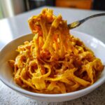 A fork lifts creamy, orange-colored One Pot Cajun Pumpkin Alfredo Pasta from a white bowl.