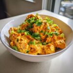 A white bowl filled with vibrant orange Oven Baked Jamaican Jerk Chicken Salad, topped with fresh cilantro and green onions.