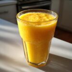A tall glass filled with a vibrant, thick Pineapple Mango Ginger Smoothie, glistening with condensation.