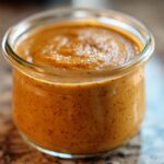 A close-up of thick, orange Pumpkin Pie Chia Pudding texture inside a small glass jar.
