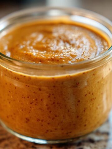 A close-up of thick, orange Pumpkin Pie Chia Pudding texture inside a small glass jar.