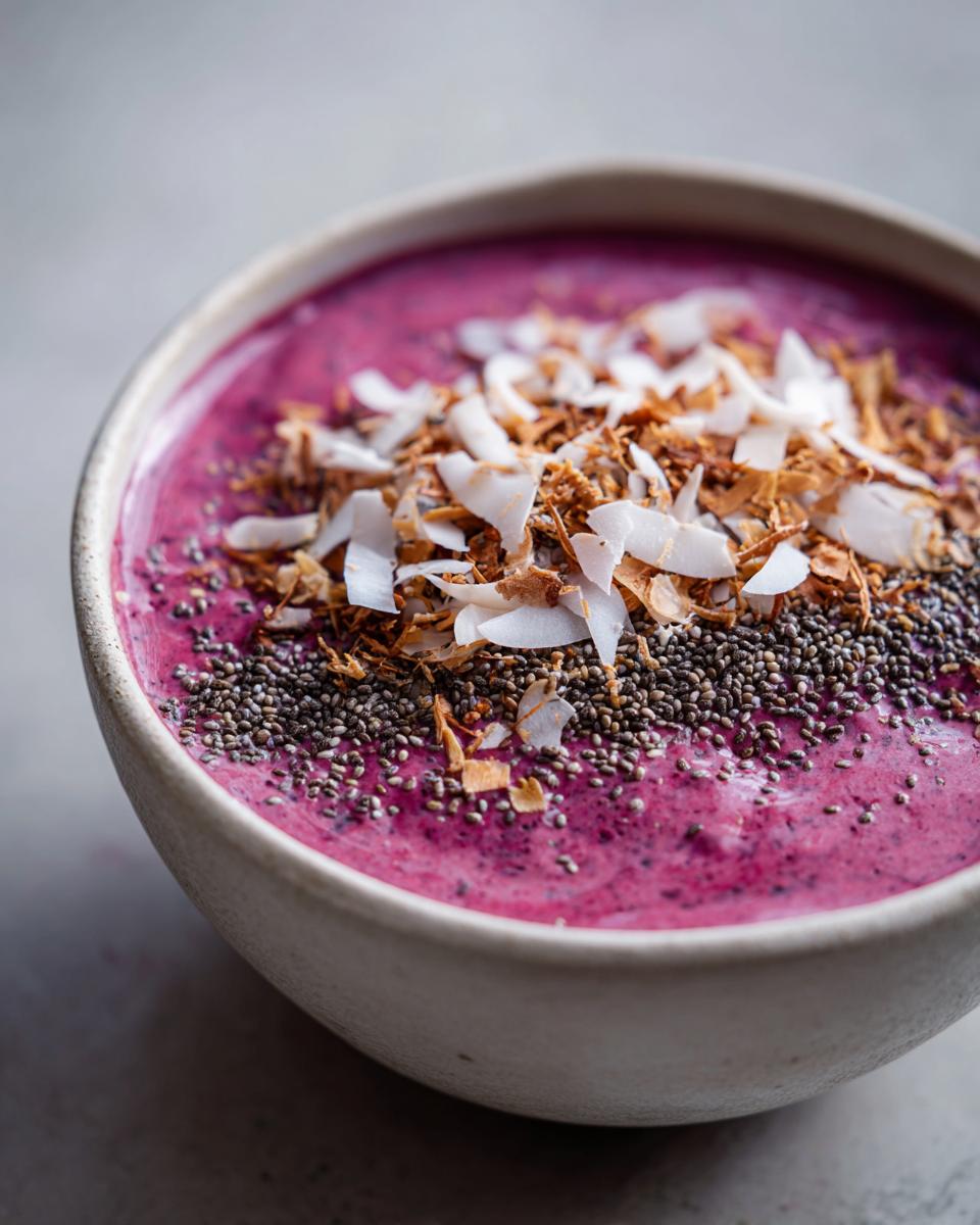 Close-up of a vibrant pink Raspberry Coconut Smoothie Bowl topped with chia seeds and toasted coconut flakes.