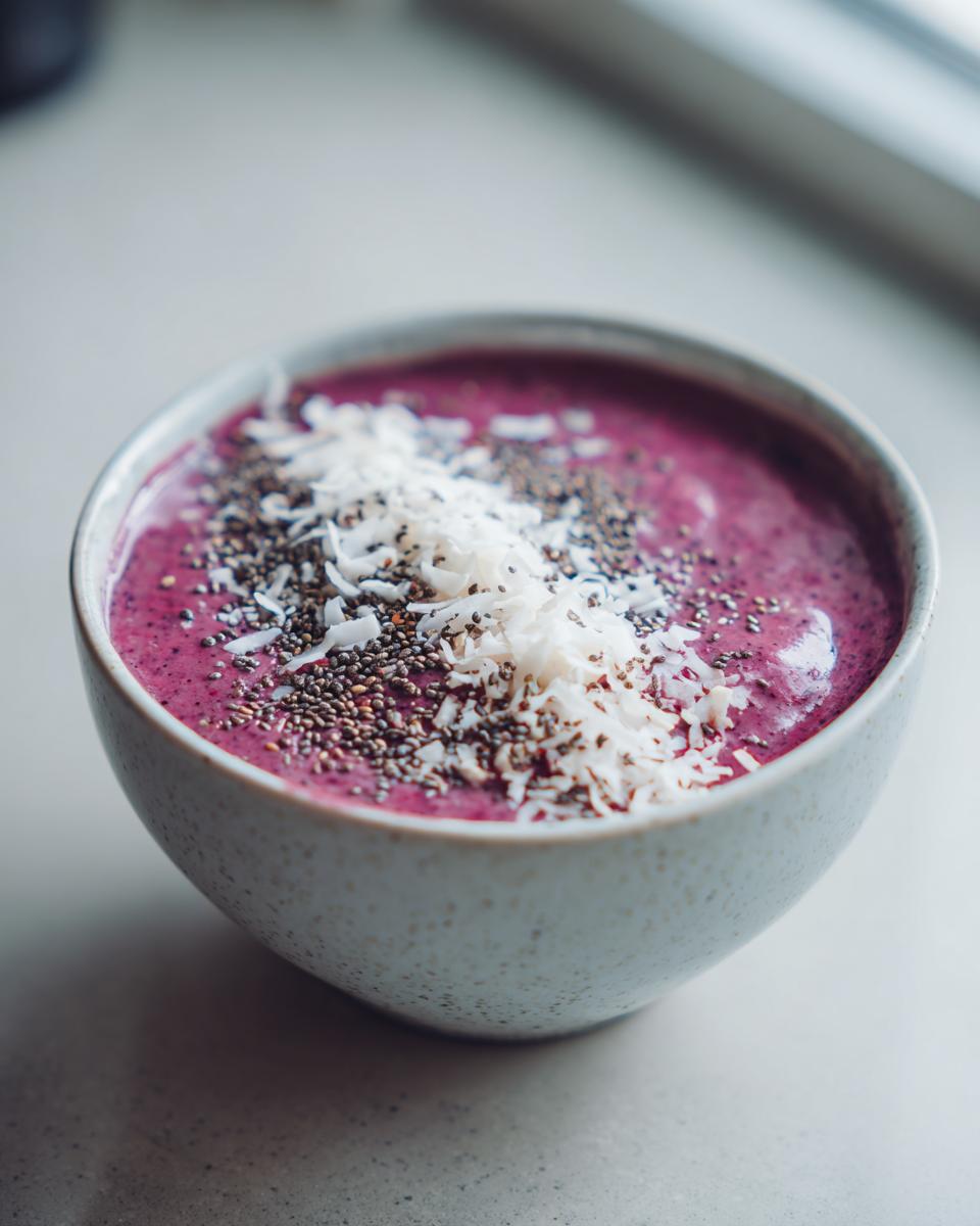 Close-up of a vibrant Raspberry Coconut Smoothie Bowl topped with toasted coconut flakes and chia seeds.