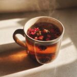 Close-up of hot Roasted Dandelion Strawberry Tea steeping in a clear mug with dried strawberries and petals.