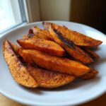 A close-up of perfectly seasoned and roasted sweet potato wedges piled on a white plate.