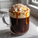 A close-up of a cold Salted Caramel Mocha Latte topped with whipped cream, caramel drizzle, and sea salt flakes.