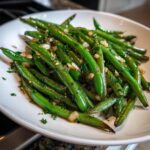 Close-up of bright green Sauteed Lemon Garlic Herb Green Beans tossed with visible minced garlic and herbs on a white plate.