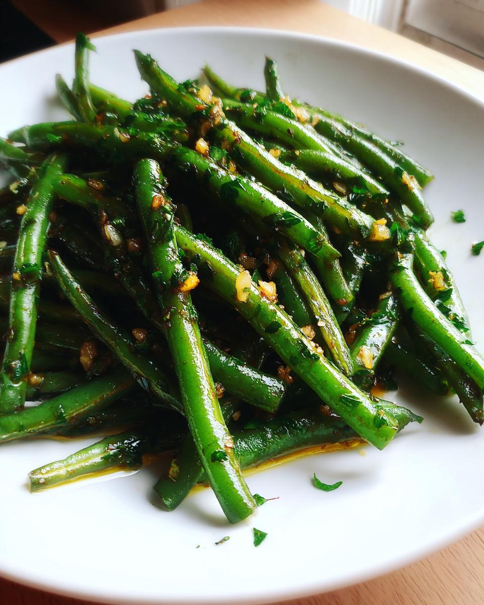 A close-up of bright green Sauteed Lemon Garlic Herb Green Beans glistening with oil and topped with minced garlic and parsley.