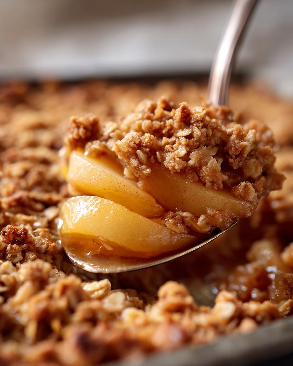 Close-up of a spoonful of Sheet Pan Maple Roasted Pear Crisp showing caramelized pear slices and crunchy oat topping.