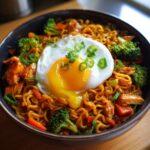 Close-up of Spicy Chili Garlic Ramen With Chicken Veggies topped with a sunny-side-up egg and green onions.