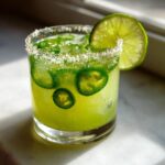 A vibrant green Spicy Jalapeno Margarita Mocktail garnished with lime and salt rim.