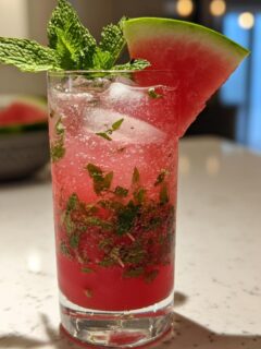 A tall glass filled with a Spicy Watermelon Mojito Mocktail, garnished with mint and a watermelon wedge.