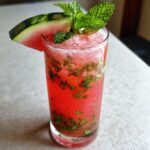 A tall glass filled with a bright red Spicy Watermelon Mojito Mocktail, garnished with mint and a watermelon slice.