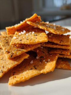 A close-up pile of golden-orange Sweet Spicy Herb Crackers sprinkled with flaky sea salt.