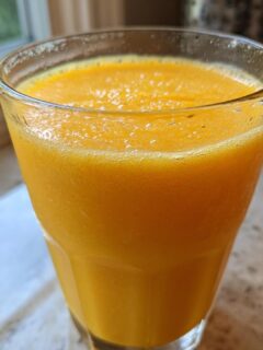 Close-up of a vibrant orange Tropical Mango Smoothie in a chilled, sweating glass.