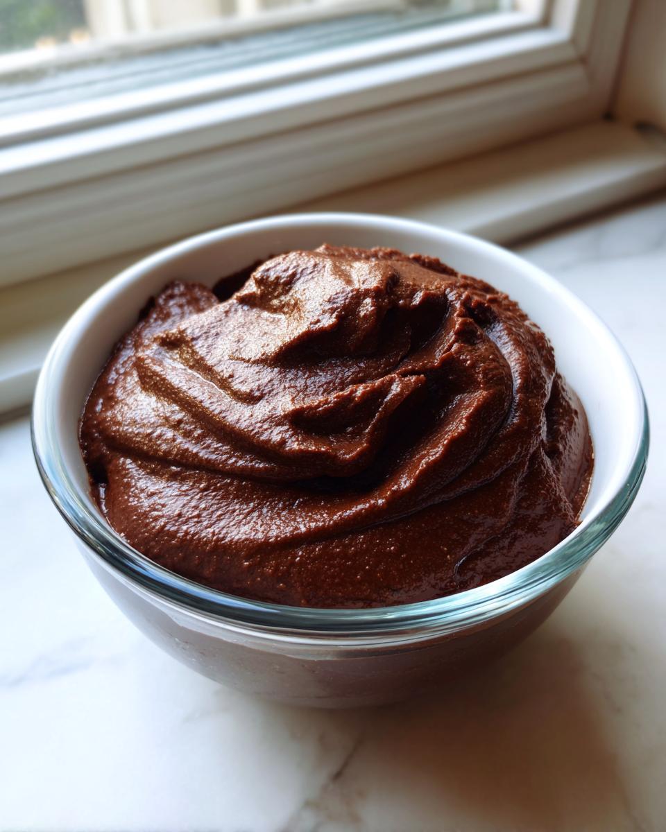 A close-up of rich, thick Vegan Chocolate Avocado Pudding swirled in a clear glass bowl.