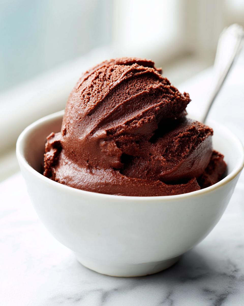 A rich, dark scoop of Vegan Chocolate Avocado Pudding served in a small white bowl on a marble surface.