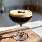 A perfectly layered Vegan Espresso Martini Mocktail in a coupe glass, topped with foam and three coffee beans.