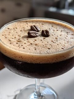 Close-up of a frothy Vegan Espresso Martini Mocktail garnished with three coffee beans.
