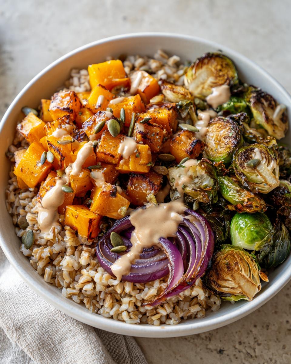 Close-up of a Vegan Fall Harvest Farro Bowl topped with roasted butternut squash, Brussels sprouts, red onion, and creamy dressing.