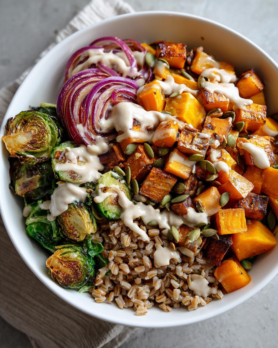 A close-up view of a Vegan Fall Harvest Farro Bowl featuring farro, roasted butternut squash, Brussels sprouts, red onion, and tahini dressing.