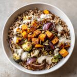 Close-up of a Vegan Fall Harvest Farro Bowl topped with roasted butternut squash, Brussels sprouts, red onion, and creamy dressing.