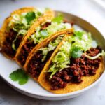 Three crispy tacos filled with spicy Jamaican jerk walnut mixture, shredded lettuce, and cilantro, ready to eat.