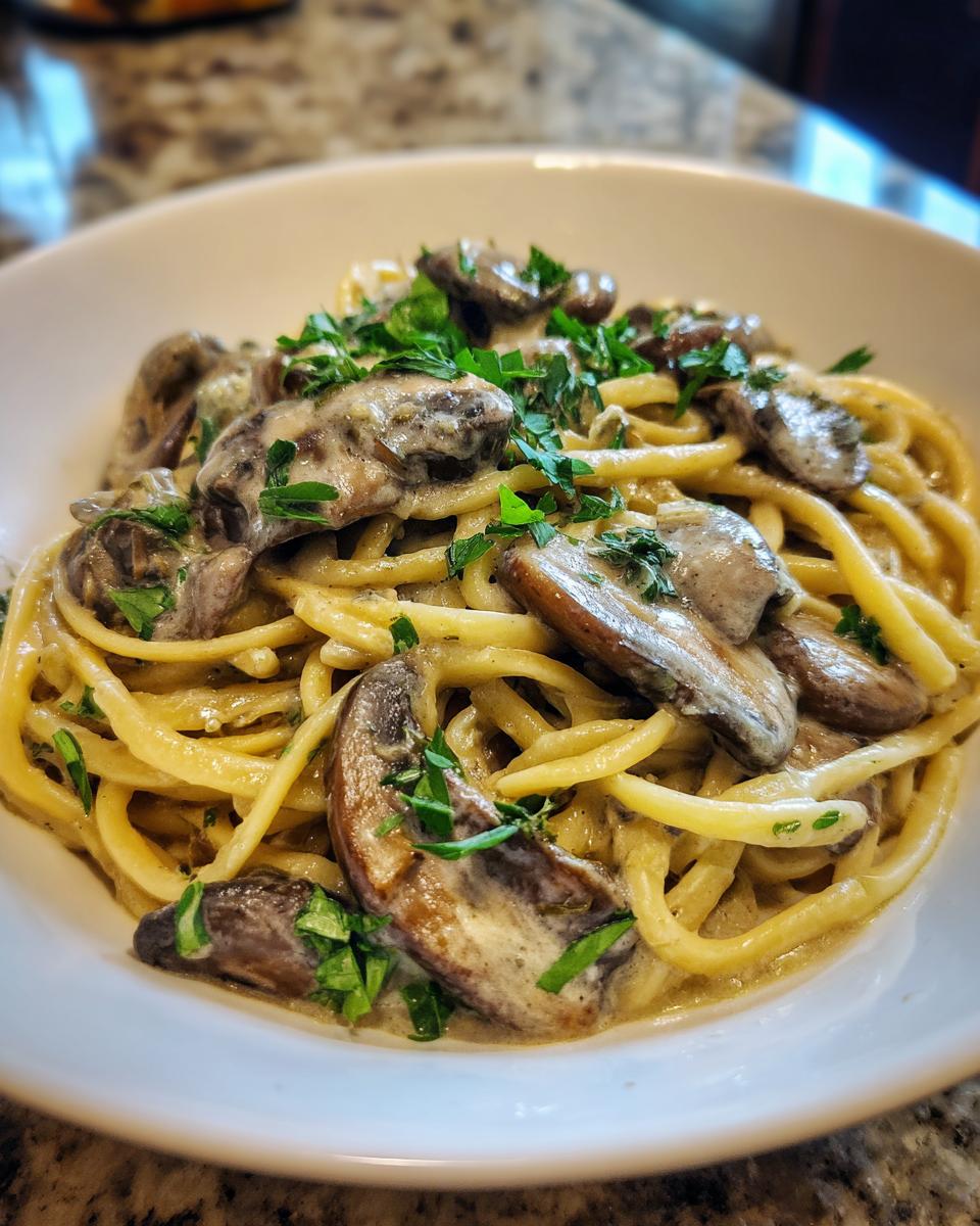 Close-up of creamy Vegan Mushroom Stroganoff served over thick pasta noodles, garnished with fresh parsley.