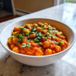A close-up of a white bowl filled with rich, orange Vegan Spicy Chickpea Curry, topped generously with fresh chopped cilantro.
