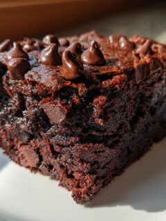 A rich, fudgy square of Vegan Sweet Potato Brownies topped with melted chocolate chips, sitting on a white plate.