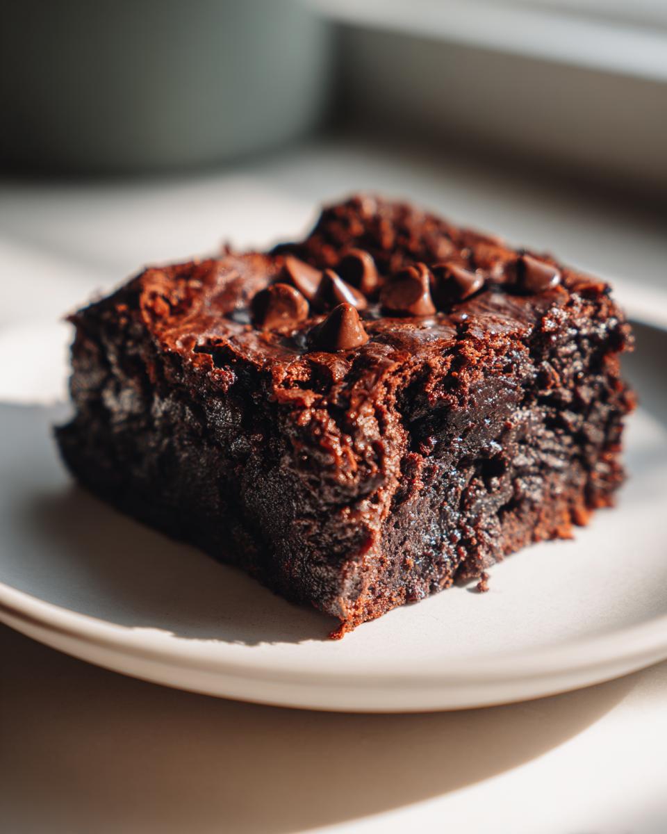 A close-up, rich, dark square of Vegan Sweet Potato Brownies topped with melted chocolate chips.