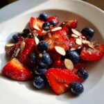 Close-up of glistening, sliced 4th Of July Strawberries mixed with blueberries, slivered almonds, and poppy seeds.
