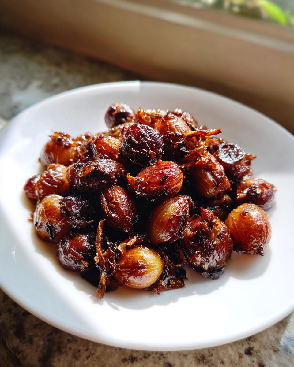 A close-up of caramelized, glossy Air Fryer Pearl Onions piled high on a white plate, catching bright sunlight.