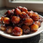A mound of caramelized, glazed Air Fryer Pearl Onions piled high on a small white plate.